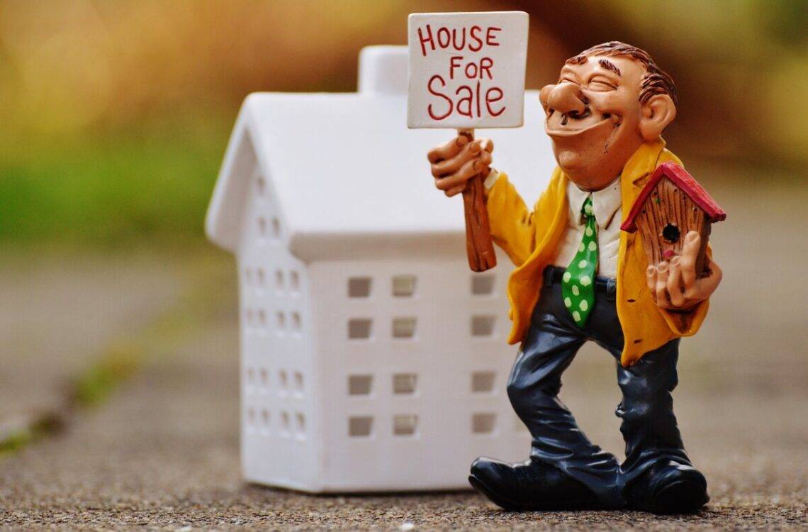 toy house with a smiling man with house for sale sign and a birdhouse