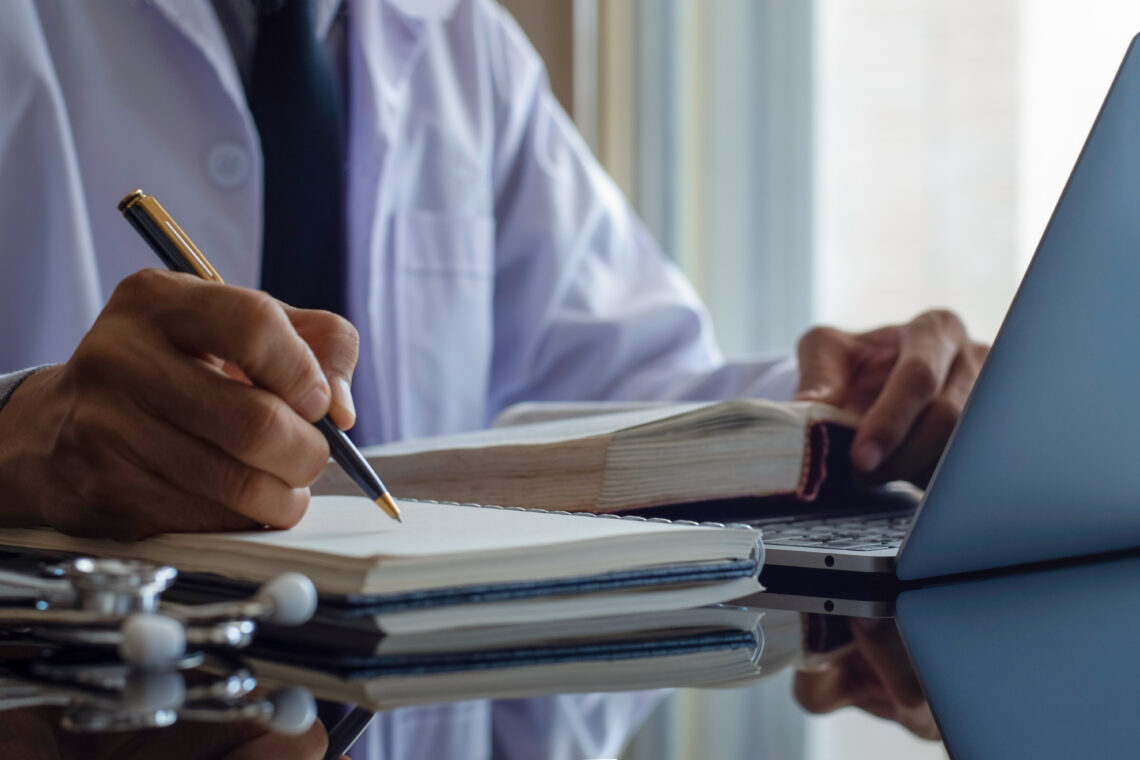 man holding pen with book and laptop