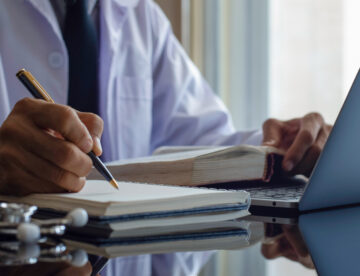 man holding pen with book and laptop