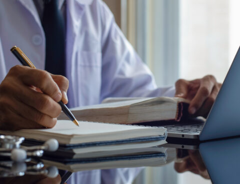man holding pen with book and laptop